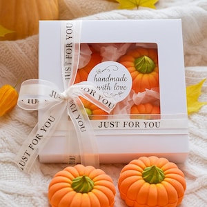 May include: A white gift box with a clear window, tied with a ribbon that says "JUST FOR YOU". Inside are orange pumpkin-shaped treats with green stems. Three pumpkin treats are in front of the box. The box has a sticker that says "handmade with love".