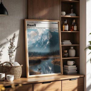 May include: A framed art print of Banff National Park, featuring a mountain range reflected in a lake. The print has a wooden frame and the text "Banff" at the top. The scene includes a deer and trees, with a cloudy sky.