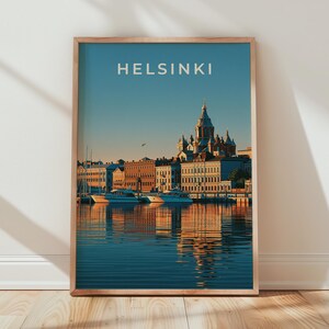 May include: A framed vertical wall art print featuring a scenic view of the Helsinki harbor at sunset. The image displays the city skyline, a prominent cathedral dome, and boats reflected in the water. The word HELSINKI is printed in white.