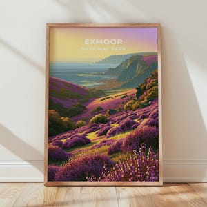 Könnte beinhalten: Ein gerahmter vertikaler Kunstdruck mit einer Landschaft des Exmoor Nationalparks. Die Szene zeigt sanfte Hügel mit violettem Heidekraut, grünem Laub und eine ferne Küste unter einem gelb-violetten Sonnenuntergangshimmel mit Text.