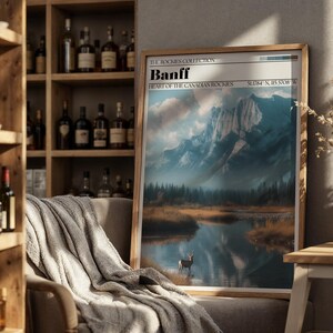 May include: Framed art print of Banff, Heart of the Canadian Rockies, featuring a mountain landscape with a lake and a deer. The print has a wooden frame and includes the coordinates 51.784 N, 115.5708 W.