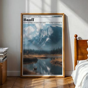 May include: A framed art print featuring a scenic landscape of Banff, part of the Canadian Rockies. The artwork showcases a mountain range reflected in a calm lake, with a deer in the water. The text "Banff" and coordinates are visible.