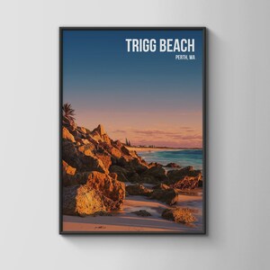 May include: A framed wall art print featuring a coastal landscape of Trigg Beach in Perth, WA. The image displays large, sunlit orange rocks in the foreground, a sandy beach, turquoise ocean water, and a gradient sky transitioning from blue to pink.