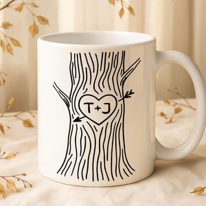 Puede incluir: Taza de cerámica blanca con un diseño de tronco de árbol negro, un corazón y una flecha. El corazón contiene las iniciales "T+J". La taza tiene un asa curva y es adecuada para bebidas frías o calientes.