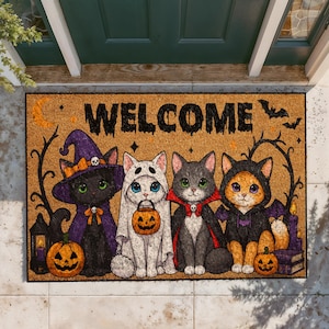 May include: A rectangular tan doormat featuring the word WELCOME in black text. The design includes four cats in Halloween costumes: a black cat in a purple witch hat, a white cat as a ghost, a gray cat as a vampire, and an orange cat in a bat hoodie.