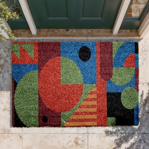 May include: Geometric patterned doormat with a vibrant design. The mat features a mix of red, blue, green, and black shapes, including circles, squares, and triangles. The design also includes a section of gold and brown stripes.