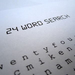 May include: A close-up of a white sheet of paper with the words "24 WORD SEARCH" printed in black. Below the title, a grid of letters is visible, suggesting a word search puzzle. The image is well-lit, highlighting the text.