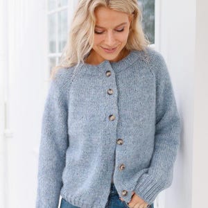 Könnte beinhalten: Hellblauer Cardigan mit rundem Ausschnitt und Knopfverschluss. Der Strickpullover hat lange Ärmel und eine strukturierte Optik. Die Knöpfe sind hellbraun.