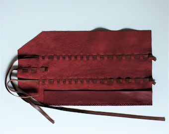 May include: A burgundy leather roll-up case with brown leather straps and stitching. The case has a flap that folds over and secures with the straps.