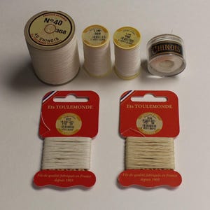 May include: Five spools of white thread, two on cards labeled "Ets TOULEMONDE" and "Fils de qualit&eacute; fabriqu&eacute;s en France depuis 1903", and three on spools labeled "AU CHINOIS", "LIN 308", and "LIN 100".
