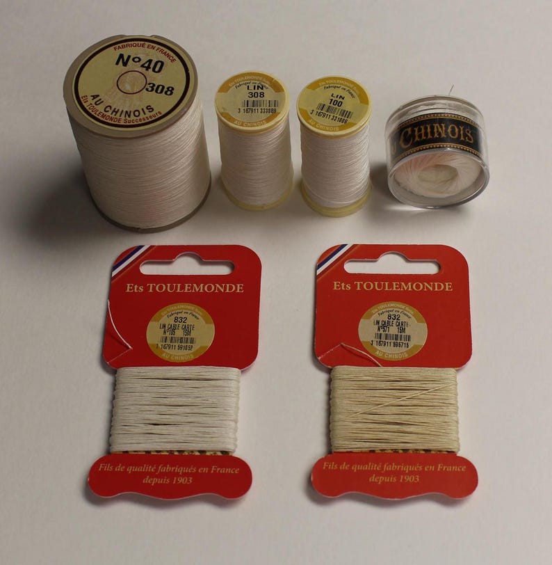 May include: Five spools of white thread, two on cards labeled "Ets TOULEMONDE" and "Fils de qualit&eacute; fabriqu&eacute;s en France depuis 1903", and three on spools labeled "AU CHINOIS", "LIN 308", and "LIN 100".