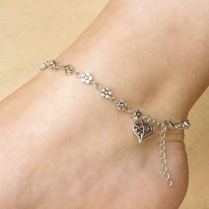 May include: Silver anklet with a floral and heart design. The anklet features small, detailed flower charms and a decorative heart pendant. The adjustable chain allows for a comfortable fit. A delicate piece of jewellery.