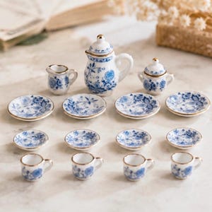 Peut inclure: Service à thé miniature en porcelaine avec motifs floraux bleus et bordures dorées. L'ensemble comprend une théière, un pot à crème, un sucrier, des soucoupes et des tasses. Les assiettes mesurent environ 2.5 cm de diamètre.