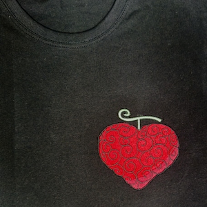 Peut inclure: T-shirt noir à col rond avec un motif rouge en forme de cœur et une tige verte. Le cœur présente un motif détaillé en volutes. Le t-shirt est en matière souple.