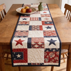 Könnte beinhalten: Ein Patchwork-Tischläufer mit roten, weißen und blauen Sternen und Streifen. Der Läufer liegt auf einem Holztisch und verleiht dem Essbereich einen patriotischen Touch. Der Tischläufer ist etwa 150 cm lang.