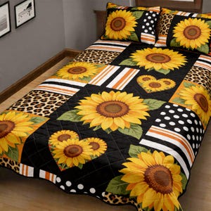 May include: A quilted bedspread and two pillowcases featuring a sunflower design. The bedspread has a patchwork pattern with sunflowers, leopard print, polka dots, and stripes in black, orange, white, and yellow. The pillowcases have a sunflower design.