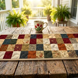 May include: A patchwork table runner in shades of red, blue, beige, and brown. A coffee mug with a floral design sits on a wooden table. The scene is set on a porch with ferns in the background.