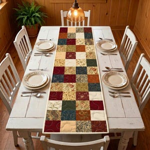 May include: A white wooden dining table set for a meal, featuring a colorful patchwork table runner. The runner has a variety of patterned squares in shades of red, green, blue, and beige. The table is set with plates, cutlery, and chairs.