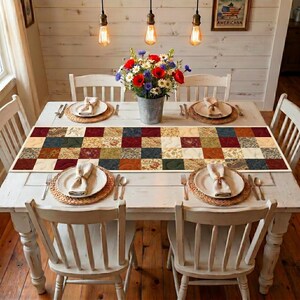 May include: A white dining table set for four with a patchwork table runner. Each place setting has a woven placemat, white plate, and folded napkin. A metal bucket holds a bouquet of flowers.