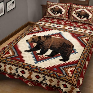 May include: A bedspread and two pillowcases featuring a brown bear design. The bedspread has a cream-colored center with a large bear illustration, surrounded by a geometric pattern in red, blue, and brown.