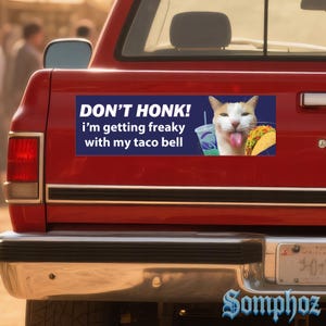 May include: A rectangular bumper sticker on a red truck features a white and orange cat with its tongue out, a Taco Bell drink, and a taco. The text reads "DON'T HONK! I'm getting freaky with my taco bell."