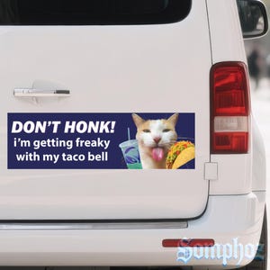 May include: A rectangular bumper sticker with a navy blue background. The text reads "DON'T HONK! i'm getting freaky with my taco bell." A cartoon cat with its tongue out is next to a taco and a drink.