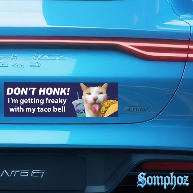 May include: A blue car bumper sticker with the text "DON'T HONK! I'm getting freaky with my taco bell." The sticker features a cat with a taco and a Taco Bell drink. The word "Somphoz" is written in a stylized font.
