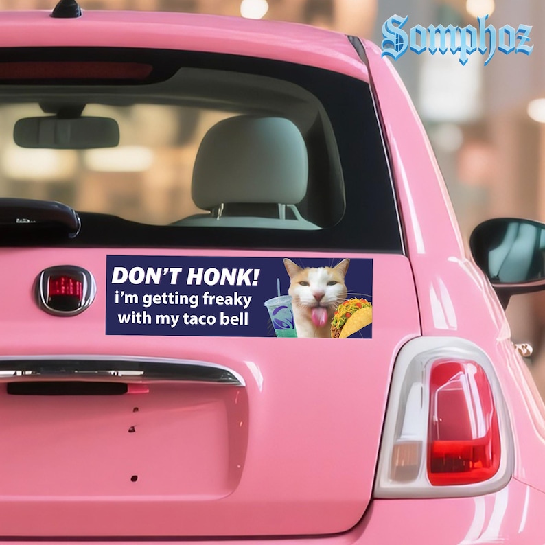 May include: A pink car with a bumper sticker that reads "DON'T HONK! I'm getting freaky with my taco bell." The sticker features a cat with its tongue out, a Taco Bell drink, and a taco.