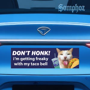 May include: A rectangular bumper sticker with the text "DON'T HONK! i'm getting freaky with my taco bell." A cartoon cat with its tongue out is next to a Taco Bell taco and drink.