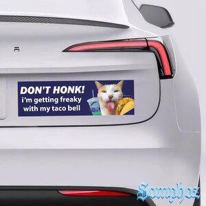 May include: A rectangular bumper sticker on a white car with the text "DON'T HONK! i'm getting freaky with my taco bell". The sticker features a cat with a Taco Bell drink and taco.