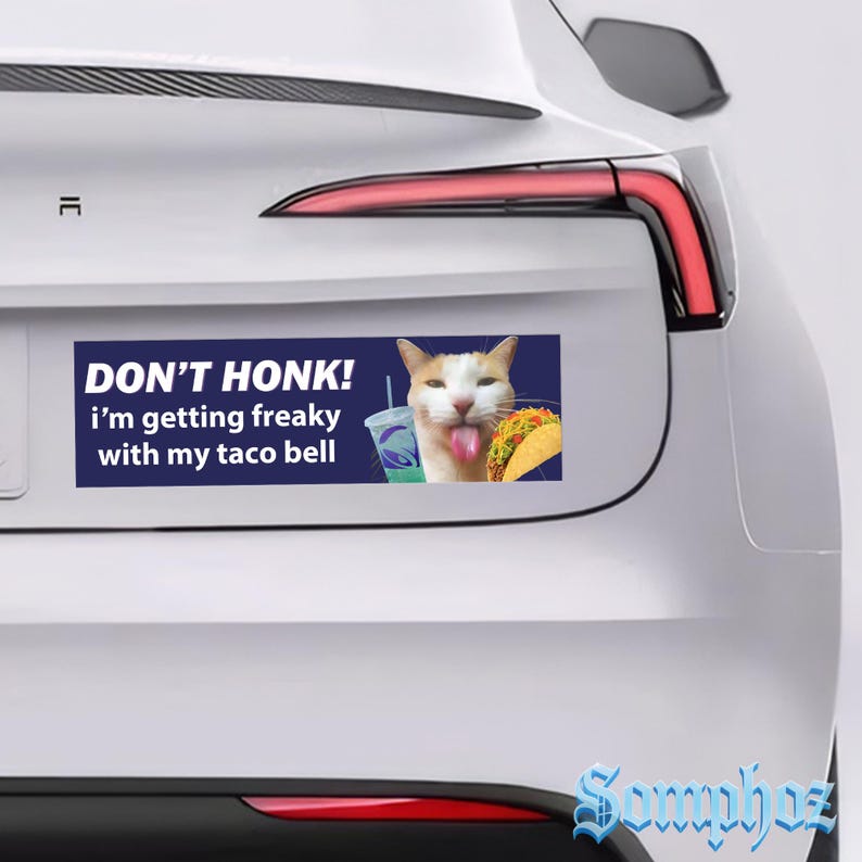 May include: A rectangular bumper sticker on a white car with the text "DON'T HONK! i'm getting freaky with my taco bell". The sticker features a cat with a Taco Bell drink and taco.