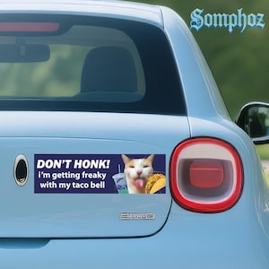 May include: A blue car bumper sticker with the text "DON'T HONK! i'm getting freaky with my taco bell". The sticker features a cat with its tongue out, a taco, and a drink.