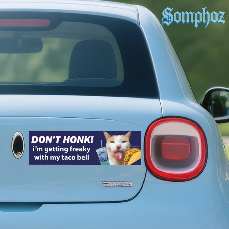 May include: A blue car bumper sticker with the text "DON'T HONK! i'm getting freaky with my taco bell". The sticker features a cat with its tongue out, a taco, and a drink.