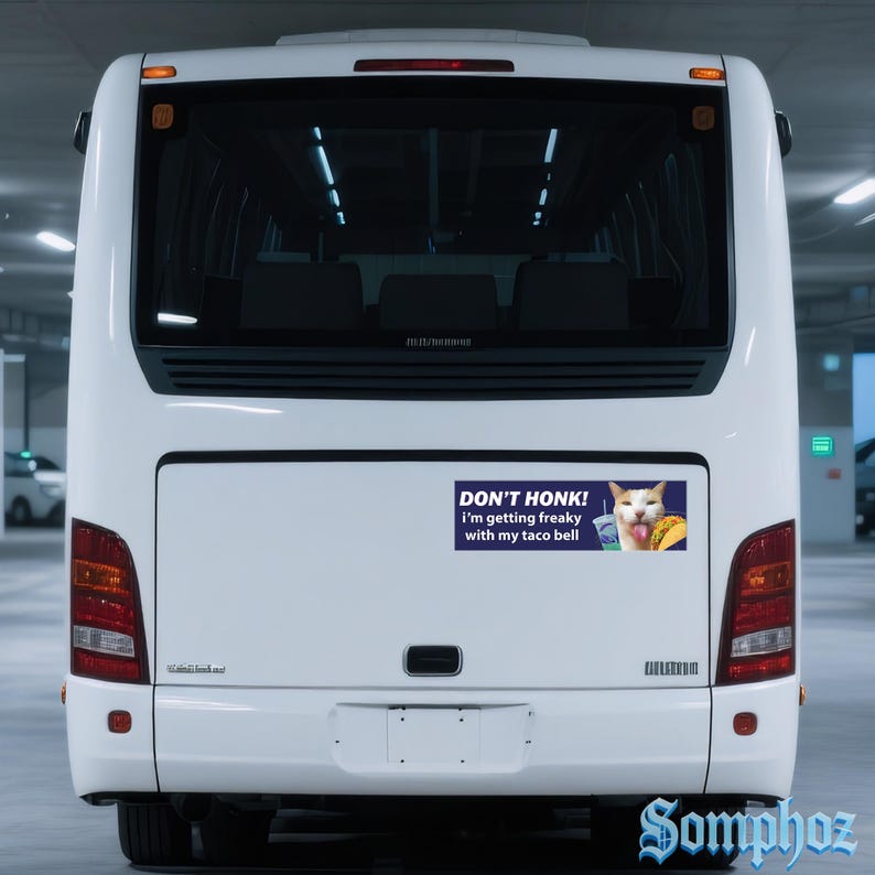 May include: White bus with a bumper sticker that reads "DON'T HONK! I'm getting freaky with my taco bell." The sticker features a cat with a taco and a drink. The bus is parked in a parking garage.