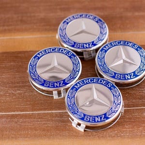 May include: Four silver Mercedes-Benz car hubcaps with blue trim and the words "Mercedes" and "Benz" in blue lettering.