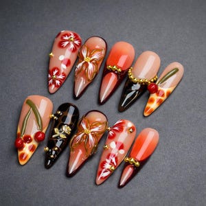 May include: A set of ten long, almond-shaped artificial nails. Each nail showcases distinct designs, such as floral patterns, cherries, and abstract art, with gold and red accents. The nails have a glossy finish and are displayed on a grey surface.