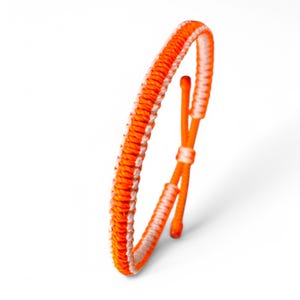 Puede incluir: Un brazalete trenzado de color naranja brillante y blanco con cierre anudado.