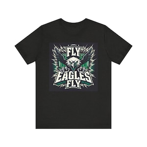 Könnte beinhalten: Schwarzes T-Shirt mit einer Grafik eines Adlers mit ausgebreiteten Flügeln. Das Design enthält die Wörter "FLY" und "EAGLES FLY" in einer kräftigen, stilisierten Schriftart mit grünen und weißen Akzenten. Das T-Shirt besteht aus einem weichen, bequemen Material.
