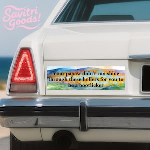 May include: A white car's rear with a bumper sticker. The sticker has a watercolor landscape design with text that reads, "Your papaw didn't run shine through these hollers for you to be a bootlicker."
