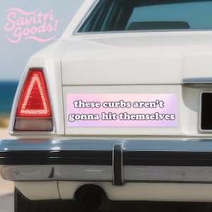 May include: A white car's rear with a bumper sticker that reads "these curbs aren't gonna hit themselves" in purple text on a pink and purple gradient background. The car has a red tail light and the Savitri Goods! logo.