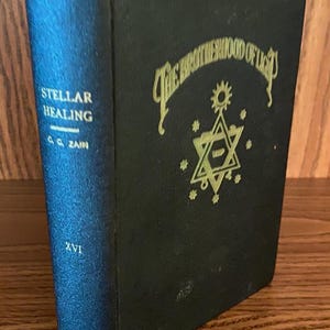 May include: A black hardback book titled Stellar Healing by C. C. Zain, volume XVI. The front cover features gold embossed text reading The Brotherhood of Light above a six-pointed star symbol surrounded by small stars and a sun icon at the top.