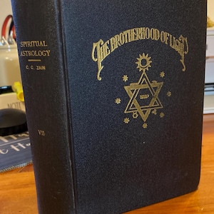 May include: A black hardback book titled The Brotherhood of Light with gold embossed lettering and a central star symbol on the front cover. The spine displays the text Spiritual Astrology, the author C. C. Zain, and the Roman numeral VII.
