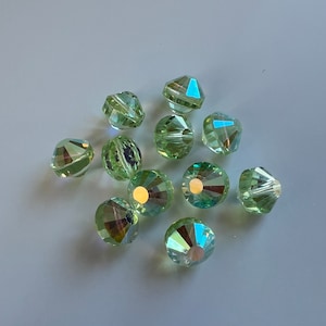 May include: A group of 10 light green faceted glass beads with iridescent shimmer. The beads are round and have a hole in the center for stringing.