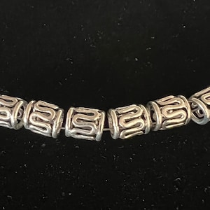 May include: Silver metal beads with an intricate design. The beads are round and have a smooth surface. They are strung together on a cord.