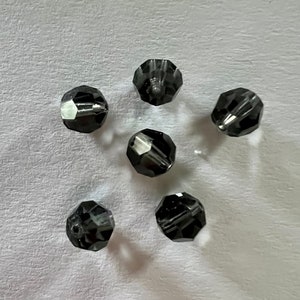 May include: Six black faceted glass beads, each with a slightly different orientation, are scattered on a white surface.