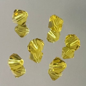 May include: Six yellow faceted glass beads with a spiral design. The beads are scattered on a white surface.