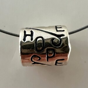 May include: Silver charm bracelet bead with the word "HOPE" engraved on it.