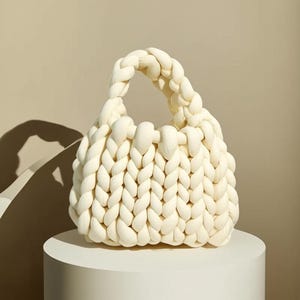 May include: A white knitted tote bag with a thick, chunky knit texture. The bag has a single handle and a rounded, slightly slouchy shape.