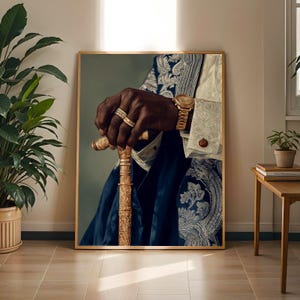 May include: A framed wall art print depicting a dark-skinned hand resting on a gold-toned walking cane. The hand wears two gold rings and a gold wristwatch. The figure is dressed in a dark blue jacket with white floral embroidery and a white shirt.