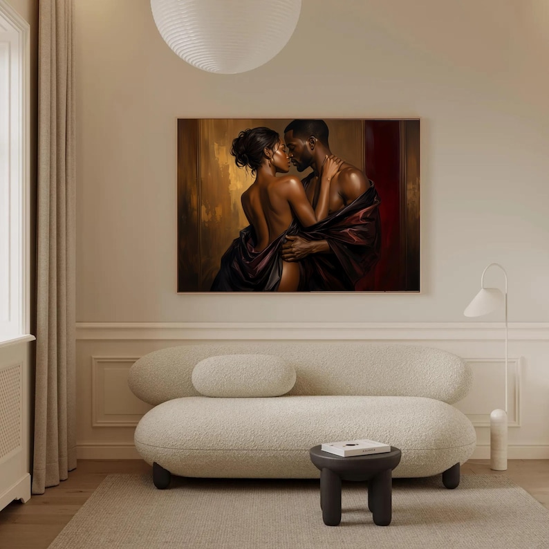 May include: A rectangular wall art print featuring a dark-skinned couple in an intimate embrace, draped in deep burgundy and black fabric against a warm, golden-brown background. The artwork is displayed in a room with a cream-coloured sofa and stool.